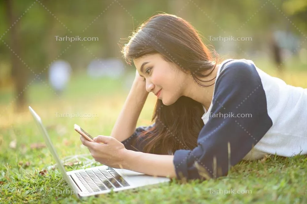 دختر جذاب در حال بازی با موبایل و لپتاپ در باغ و فضای باز