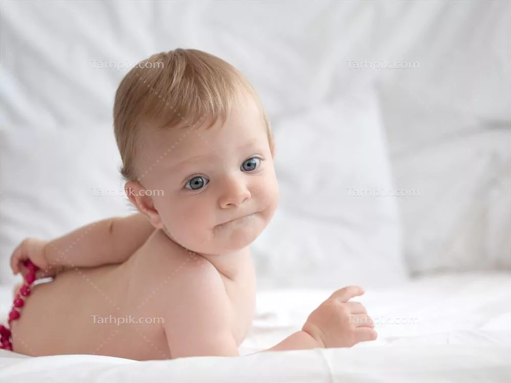 کودک نوزاد در حال بازی بر روی تخت با گوی های رنگی