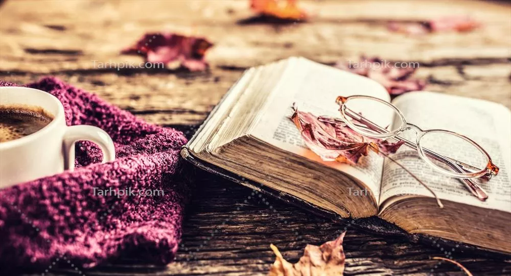 فنجان قهوه، کتاب قدیمی، عینک و برگهای پاییزی بر روی میز