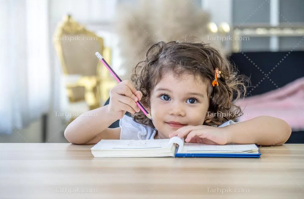 دختر کوچولوی دوستداشتنی در حال انجام تکالیف مدرسه در خانه با کتاب و رنگها