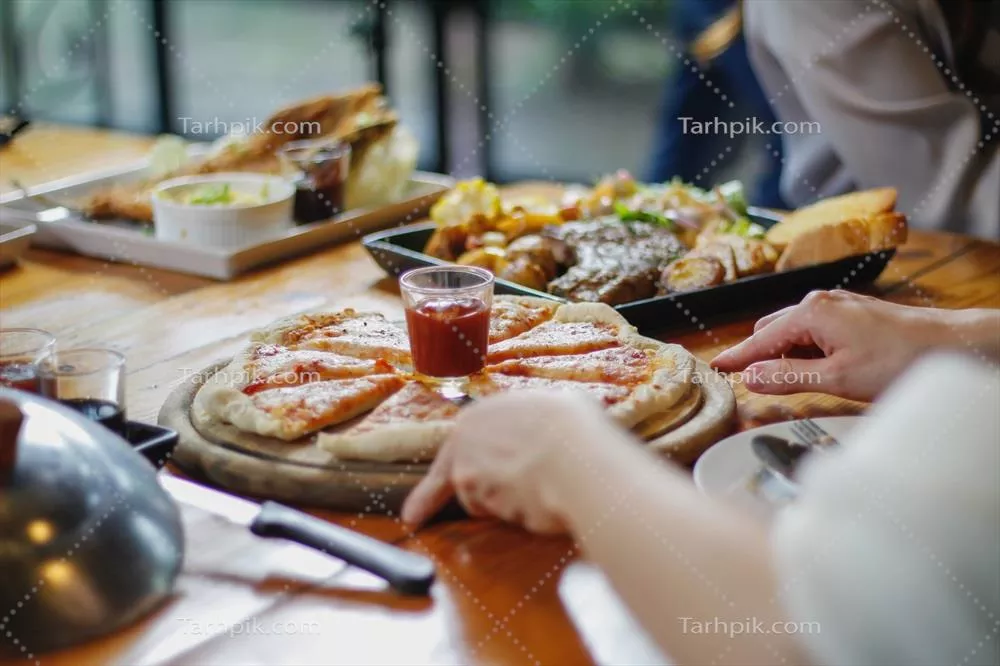 زنی جوان خوشحال از دیدن غذا بر روی میز و انتخاب منوی پیتزا برای خوردن