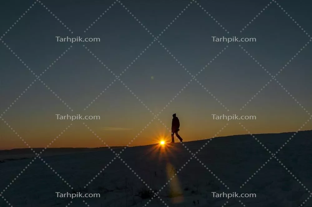 سکوت غروب: سایه مردی در حال قدم زدن در فصل زمستان با خورشید غروب در پسزمینه کوهها