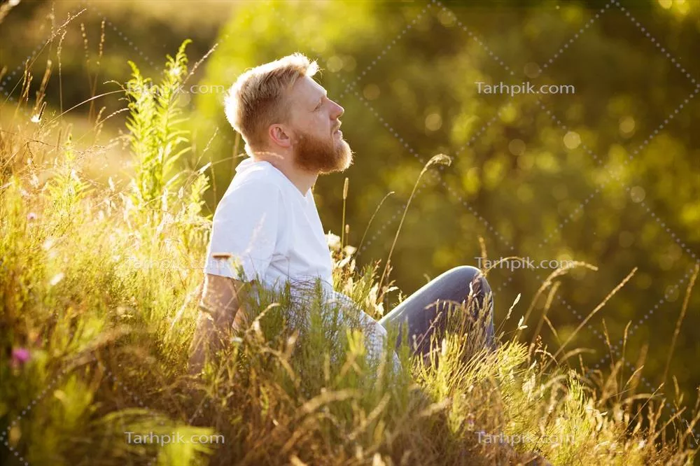 مرد خوشحال نشسته بر روی چمن و در حال رویاپردازی