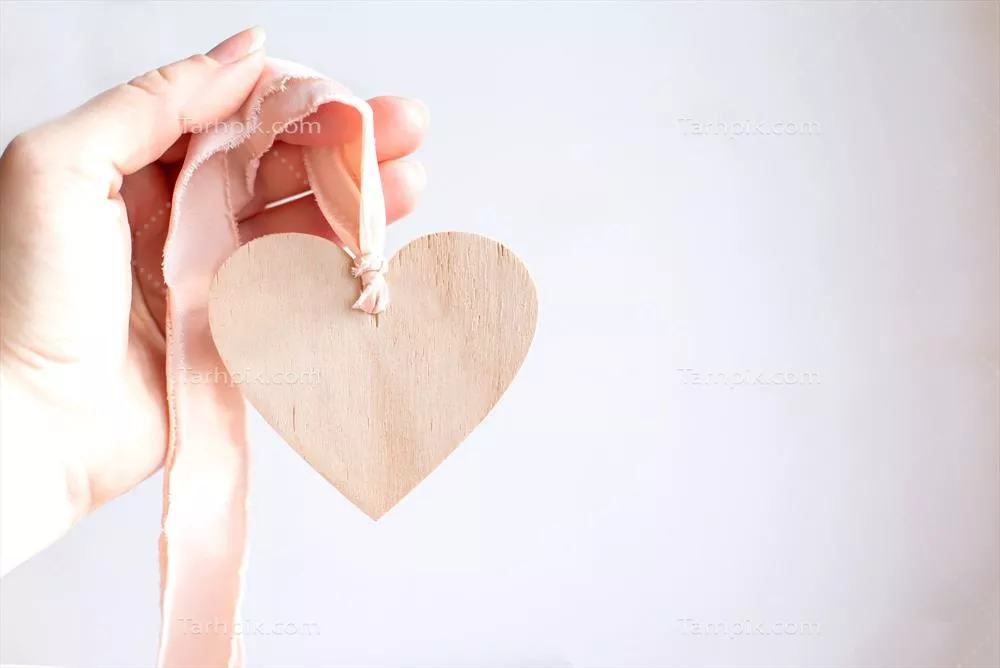 دست holding قلب چوبی با روبان صورتی و فضای خالی برای نوشتن