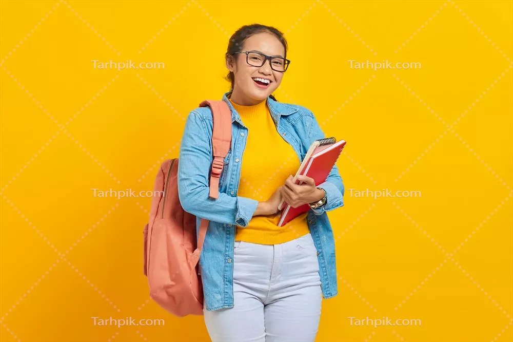 پرتره یک زن جوان آسیایی شاد در لباسهای غیررسمی با کولهپشتی و کتاب در دست بر روی پسزمینه زرد