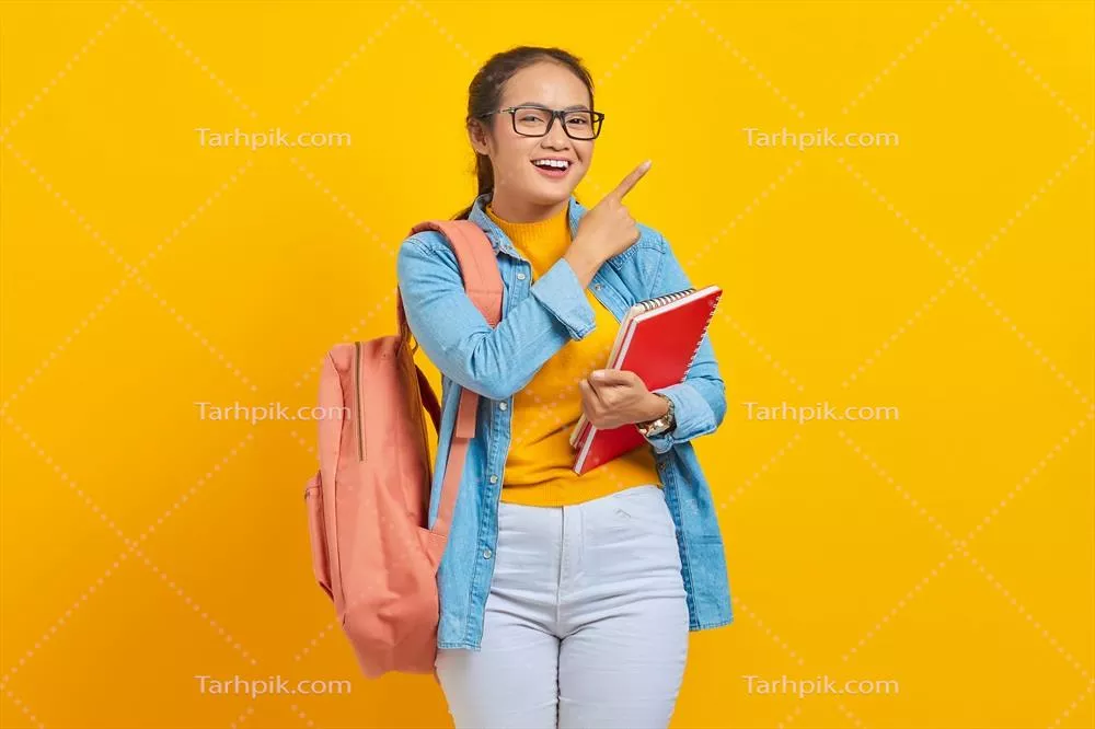 پرتره زن جوان آسیایی خوشحال در لباس casual با کولهپشتی و کتاب در دست بر روی پس زمینه زرد
