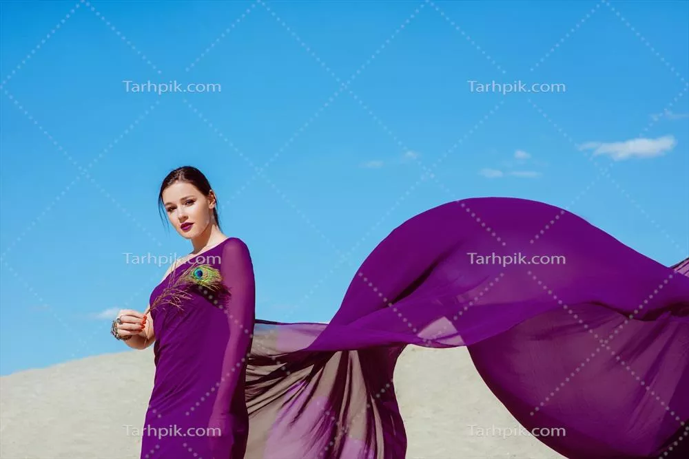زن زیبا و شگفت انگیز قهوه ای با پر طاووس در پارچه بنفش در بیابان با سبک مد مدی orientali