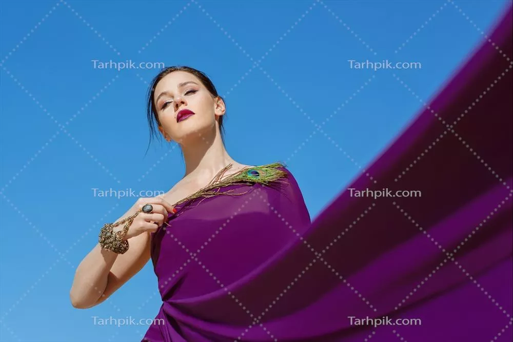 زن زیبای فوقالعاده با موهای قهوهای و پر طاووس در لباس بنفش در بیابان به سبک مد شرقی هندی