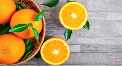 نمای بالای پرتقال‌های تازه در سبدها و پرتقال‌های نصف‌شده بر روی پس‌زمینه چوبی