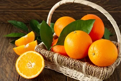 پرتقال های تازه و آبدار با برگ های سبز در سبد روی پس زمینه چوبی