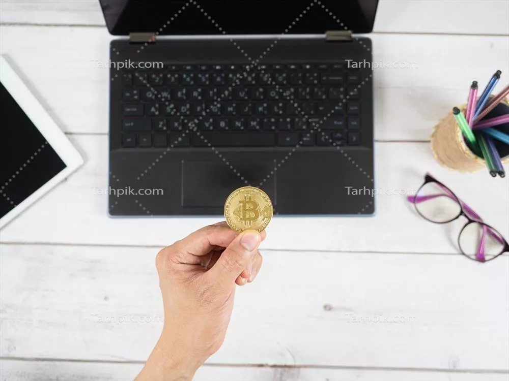 نگه داشتن بیت کوین طلا در کنار تلفن همراه و لوازم دیجیتال روی میز چوبی