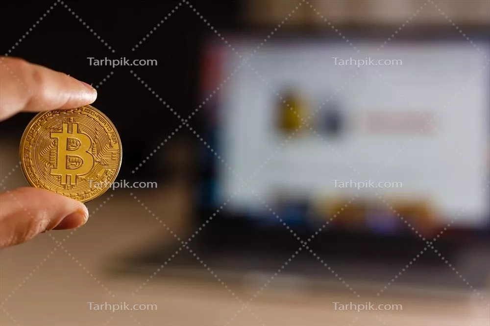 نگهداری بیت کوین طلا در دستان انسان در پس زمینه لپتاپ روی میز سفید