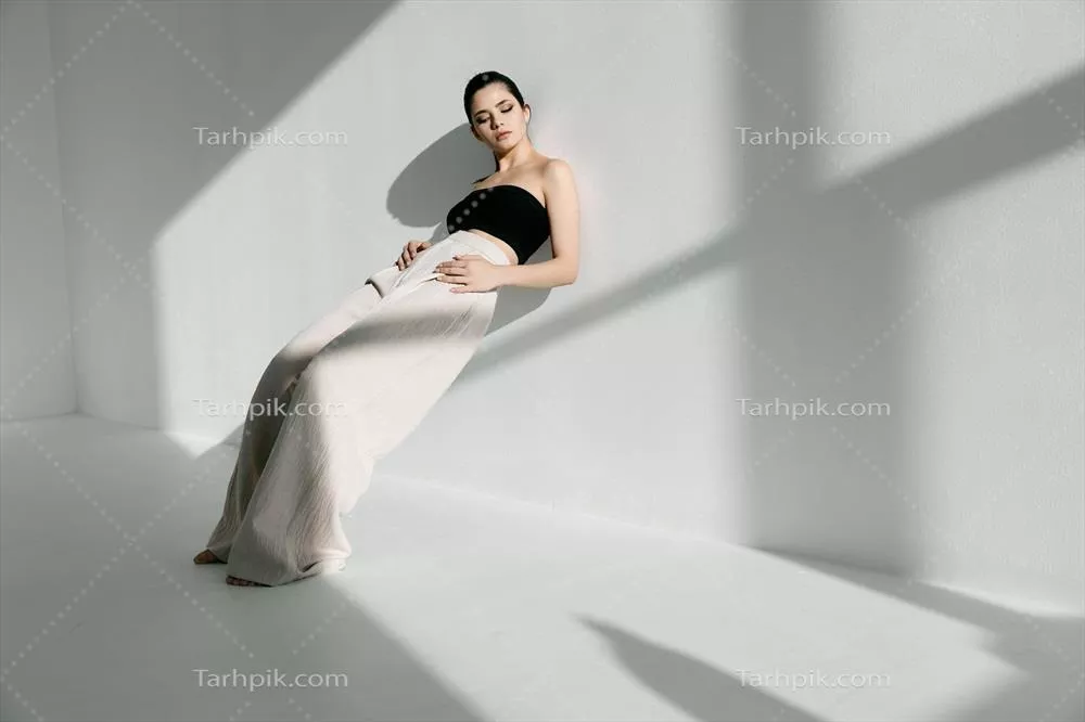 زنی مد روز در اتاقی روشن که به دیوار تکیه داده و نور خورشید بر او می‌تابد