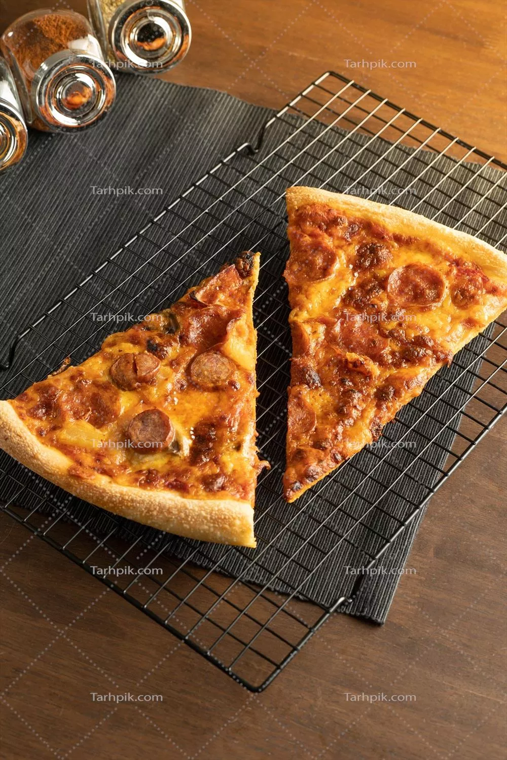 عکس نزدیک بر روی دو پیتزا با فلفل دلمه‌ای روی قفسه خنک کننده و ادویه‌جات تازه