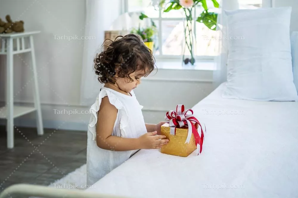 دختر کوچک زیبا و شاداب که پس از دریافت جعبه هدیه در تخت خواب از والدینش خوشحال است