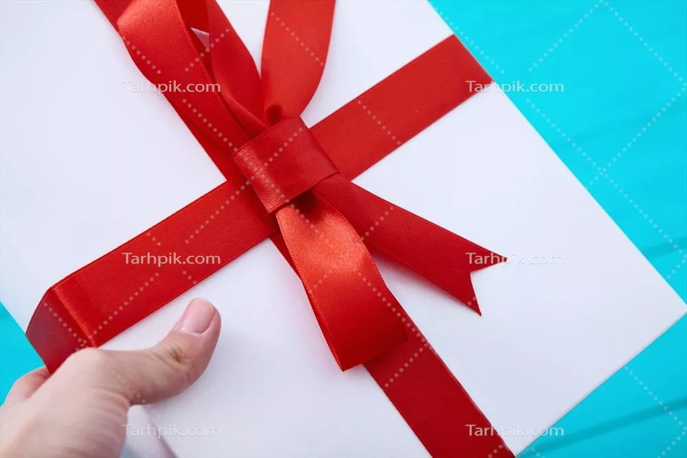 دست زنانه با ناخن‌های قرمز روی جعبه هدیه بر روی پس‌زمینه چوبی آبی - نمای فوقانی و فضای خالی