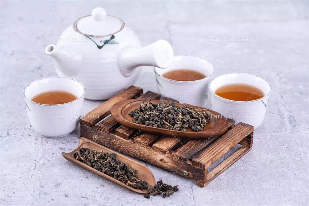 چای داغ در یک کتری سفید و فنجانها بر روی توری با پسزمینه روشن و بتن خاکستری