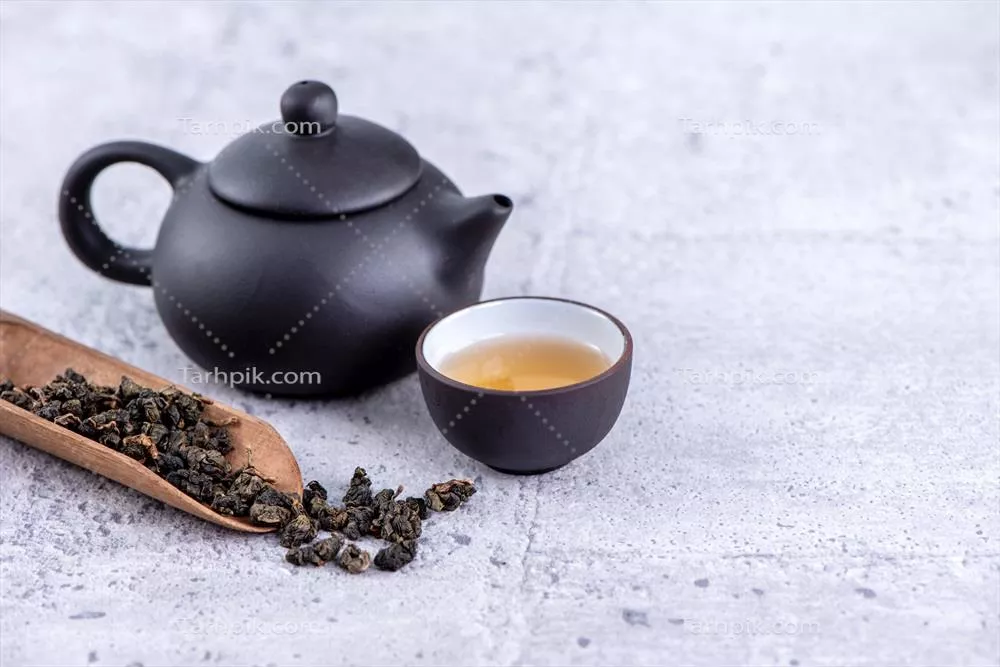 چای داغ در قوری مشکی و فنجانها با برگهای چای خشک بر روی زمینه سیمانی روشن