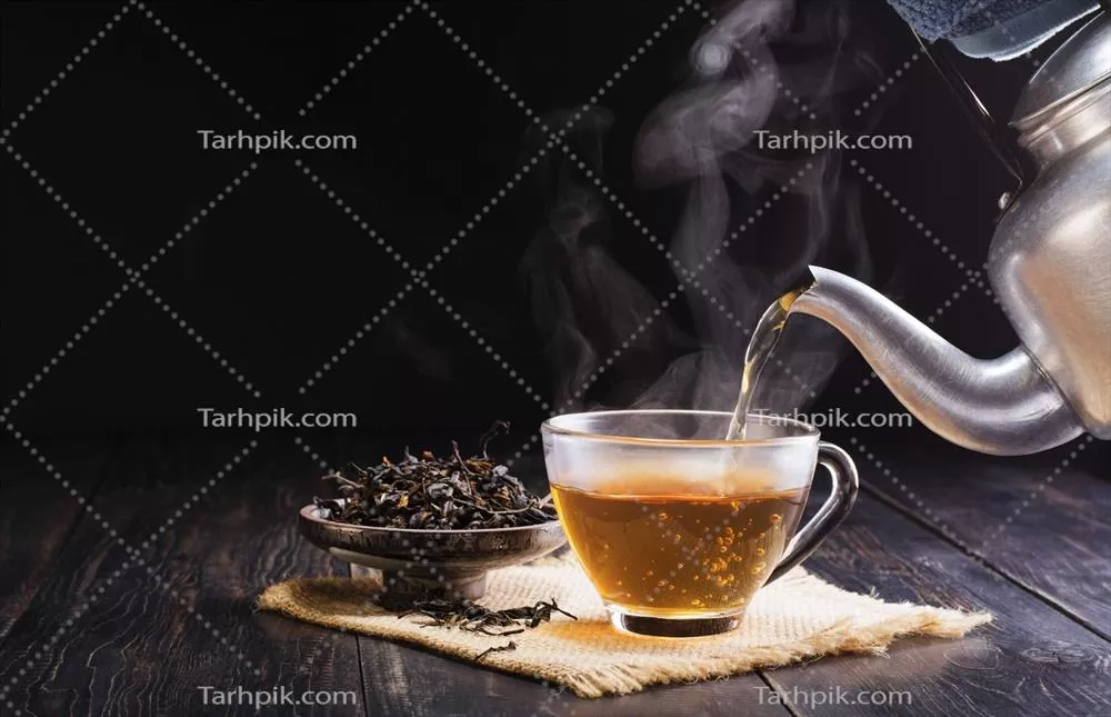 چای داغ گیاهی در فنجان شیشهای ریخته میشود بر روی میز چوبی سیاه در پسزمینه تاریک زیر نور آفتاب صبحگاهی