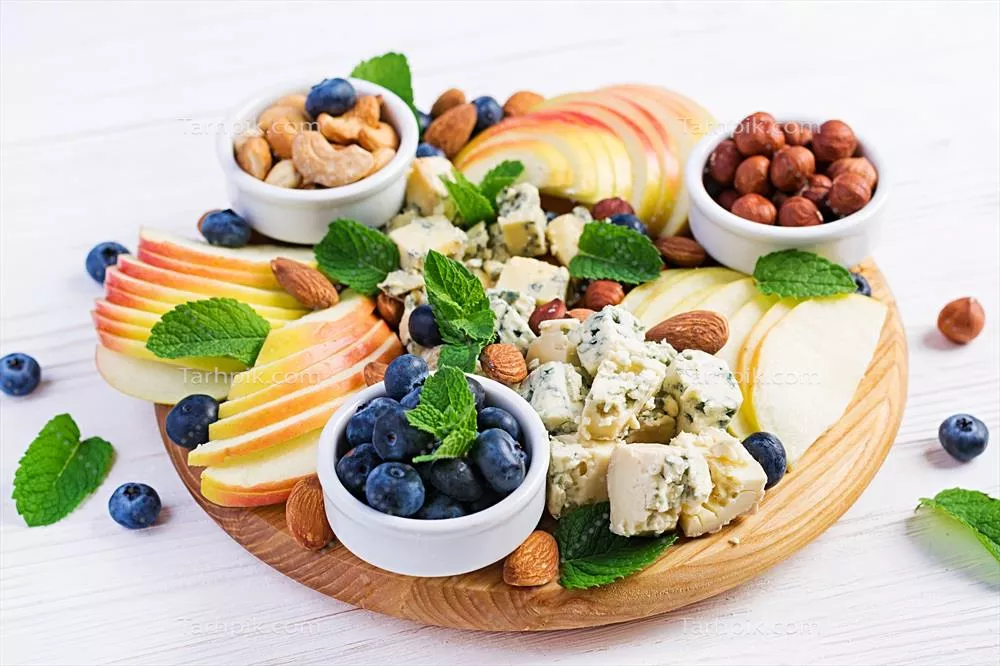 پلاتر پنیر با انواع پنیرها، توتز blueberries، سیبها و آجیلها بر روی میز سفید - پلاتر پنیر ایتالیایی و میوه ها