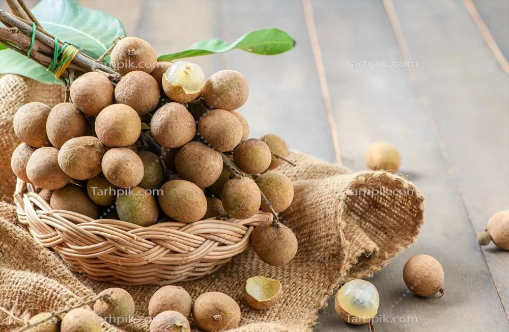 میوه تازه لانگان با برگها در سبد بامبو روی چوب