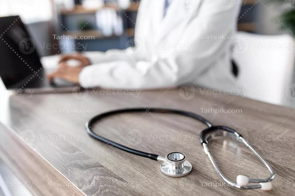 استتوسکوپ و پزشک در حال کار با لپتاپ در کلینیک: مفاهیم پزشکی و بهداشتی