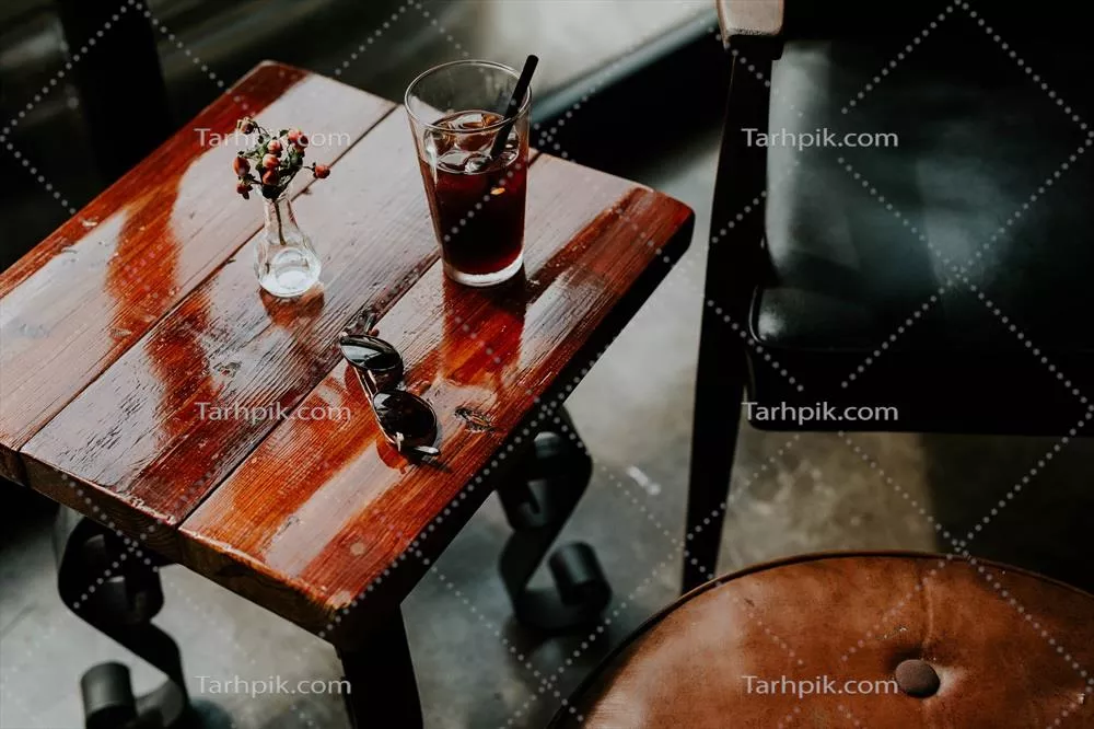 عکس نوشیدنی و عینک آفتابی بر روی میز قهوه ای مربع شکل