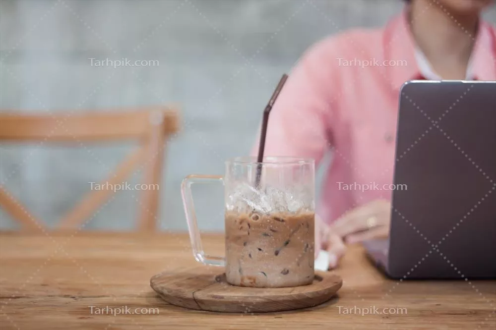 عکس زن مشغول به کار با لپ تاپ در کافی شاپ در حال نوشیدن قهوه یخ زده
