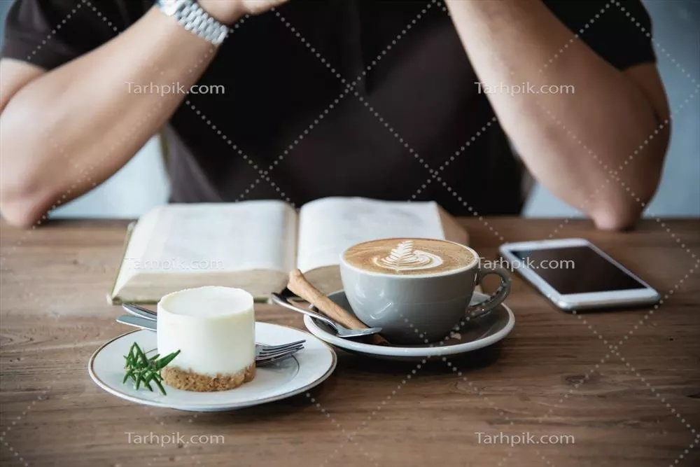 عکس مرد آسیایی آرام با قهوه در دست و کتابی در کافی شاپ مدرن نشسته است