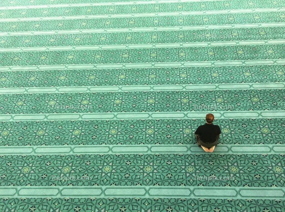 عکس نماز خواندن فردی تنها در مسجدی با فرشهای سبز