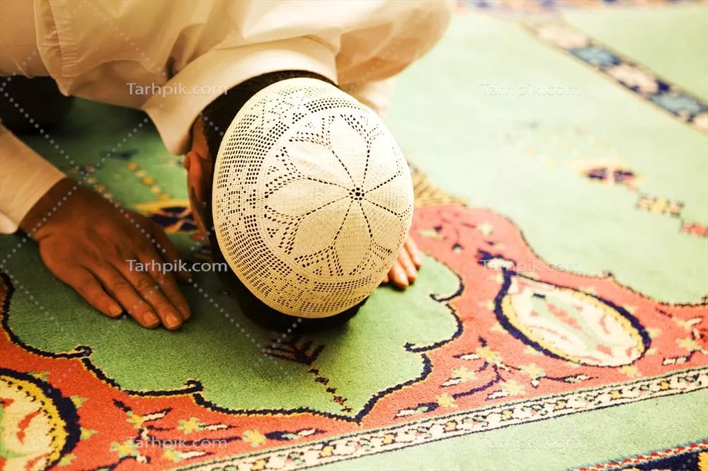 عکس فردی در حال انجام نماز بر روی فرش در مسجد با کلاه کیپا