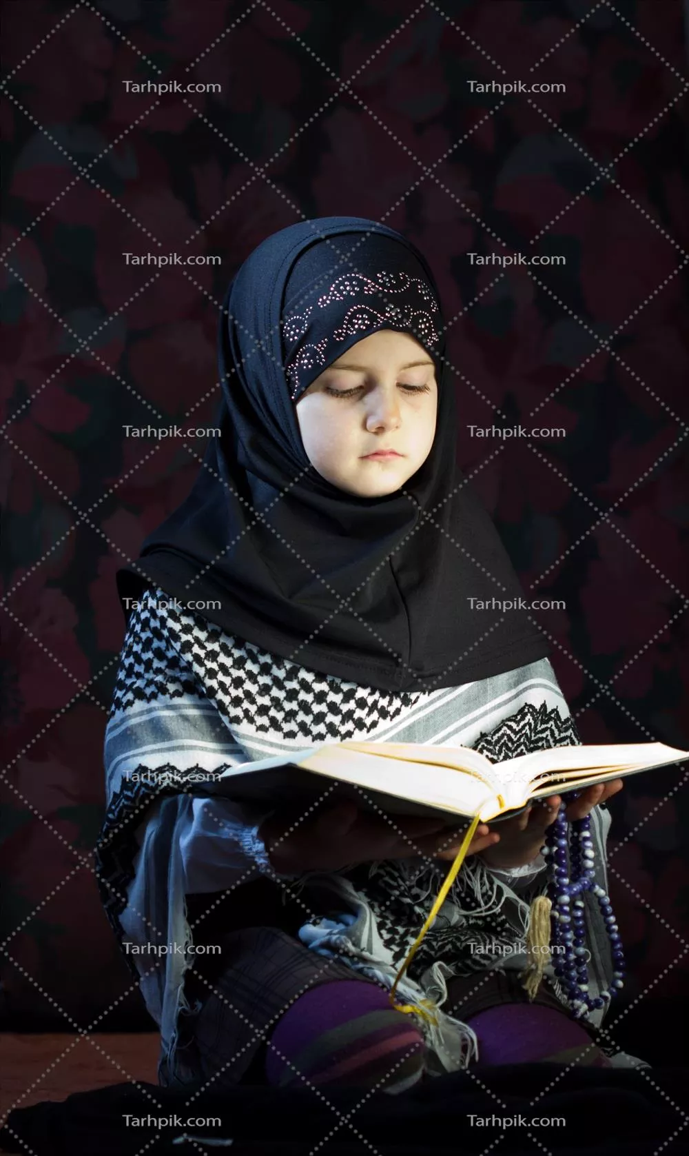 عکس کودک مسلمان محجبه در حال خواندن کتاب مذهبی با تمرکز و آرامش