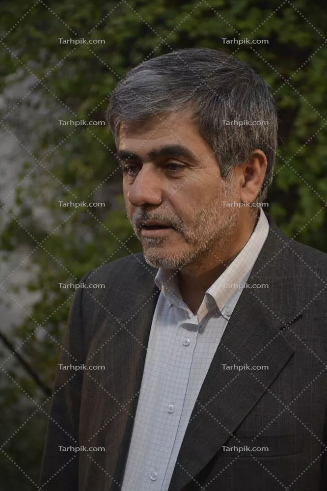 عکس تصویری از مردی با کت و پیراهن در فضای باز با پس زمینهای سبز