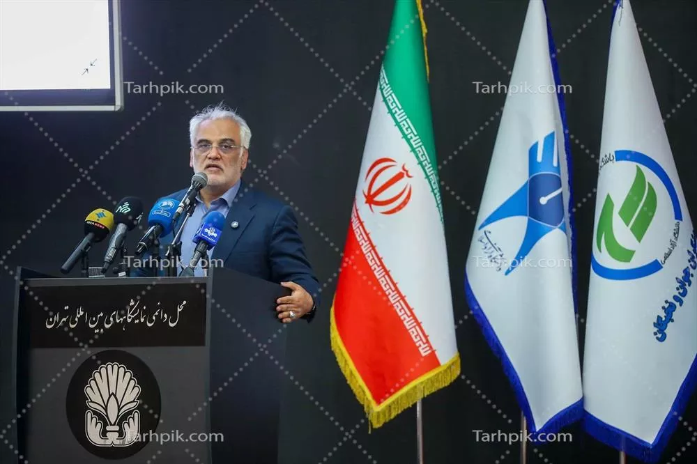 عکس سخنرانی در مراسم رسمی همراه با پرچمهای ملی و سازمانی