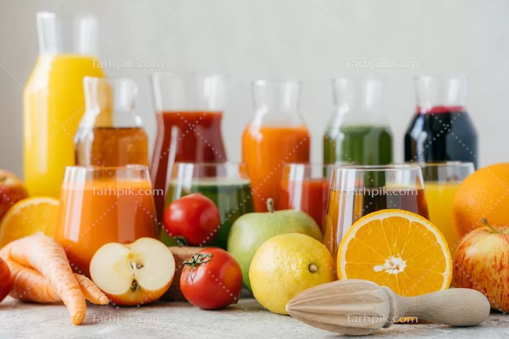عکس نمایی افقی از میوهها و سبزیجات تازه روی میز سفید با شیشههای آبمیوه و آبچکان نارنجی - مفهوم نوشیدنیهای سالم و گیاهی