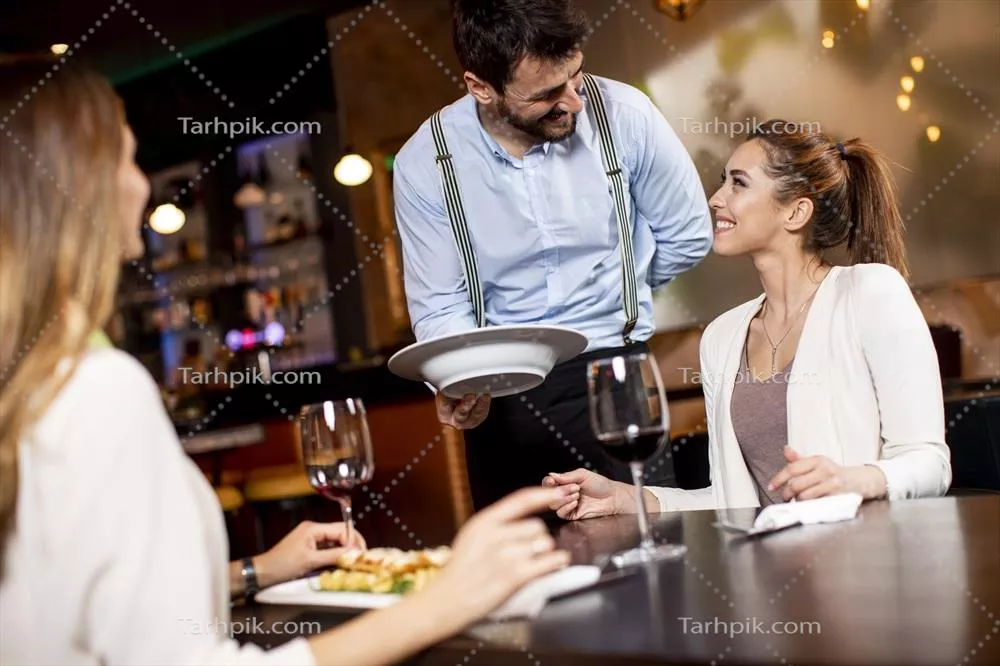 عکس خدمتکار جوانی که در رستوران به مشتریان زن غذا سرو می‌کند