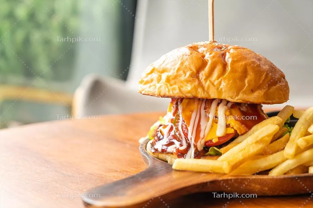 عکس همبرگر گوشت گوساله با پنیر و سس بر روی بشقاب چوبی