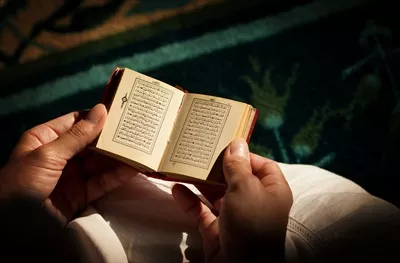 عکس مسلمان در حال خواندن قرآن کوچک با دقت و تمرکز